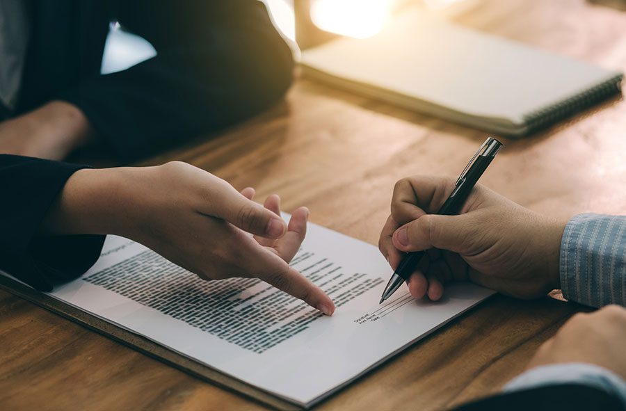 two-people-signing-paperwork-at-a-wooden-desk