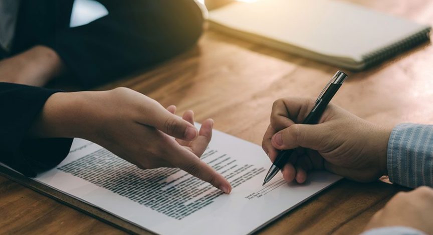 two-people-signing-paperwork-at-a-wooden-desk
